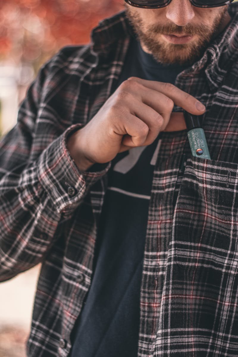 Close-up of a man putting a CBD product into his shirt pocket on a fall day.